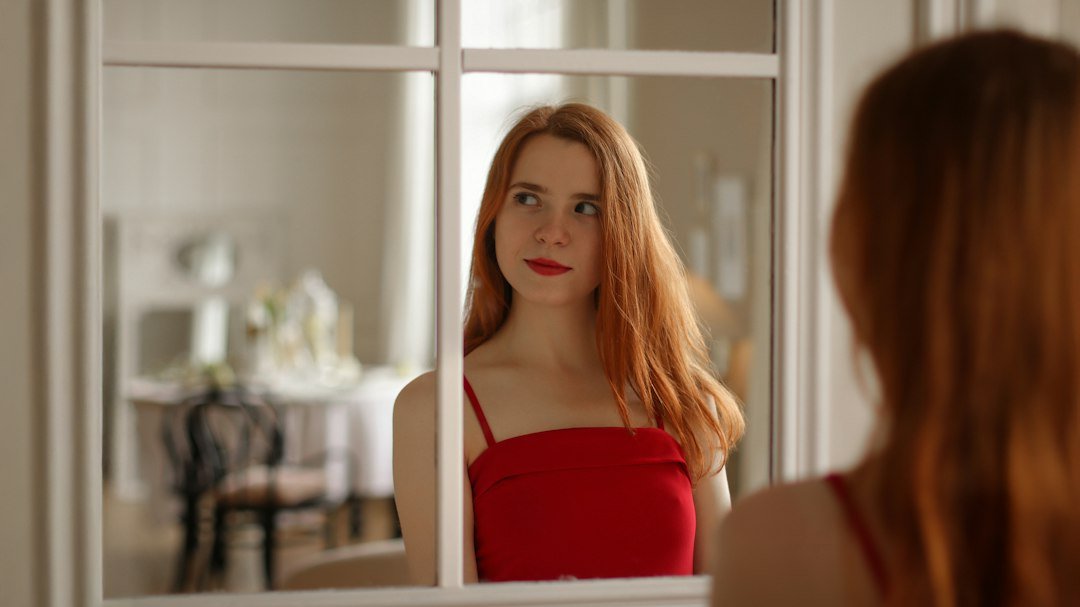 Young woman with red hair looks in mirror
